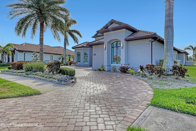 mediterranean / spanish home with a tile roof, curved driveway, and stucco siding
