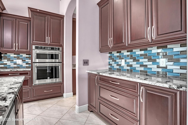 kitchen featuring tasteful backsplash, light tile patterned floors, arched walkways, double oven, and light stone countertops