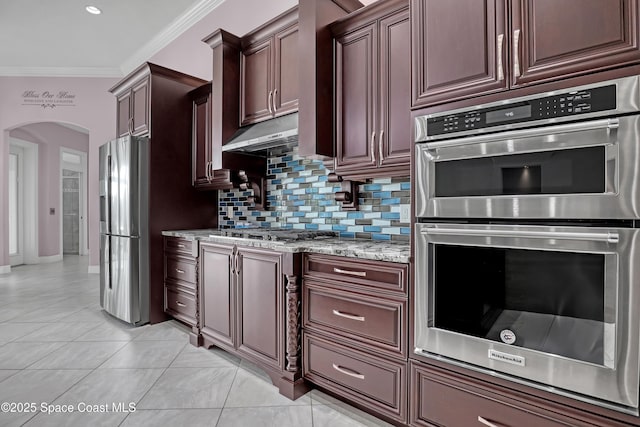 kitchen with crown molding, arched walkways, light stone counters, stainless steel appliances, and backsplash