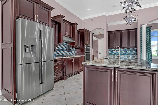 kitchen with crown molding, arched walkways, a sink, stainless steel appliances, and backsplash