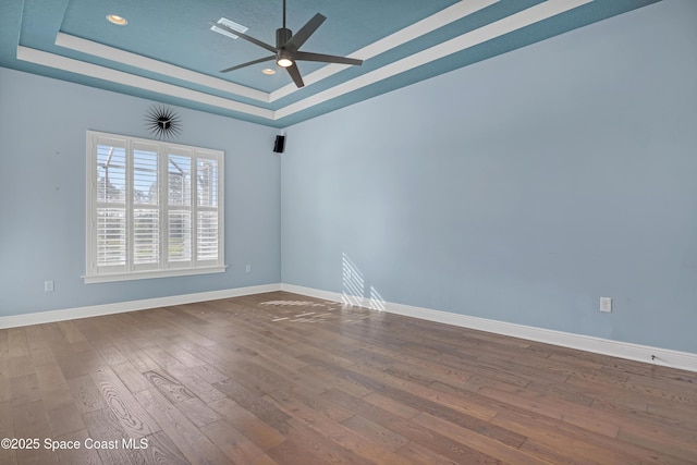 spare room featuring dark wood-type flooring, baseboards, a ceiling fan, and a raised ceiling