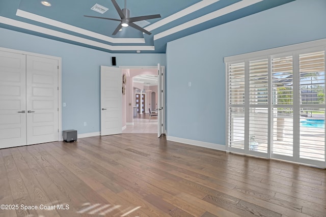 unfurnished bedroom with visible vents, baseboards, arched walkways, a tray ceiling, and wood finished floors