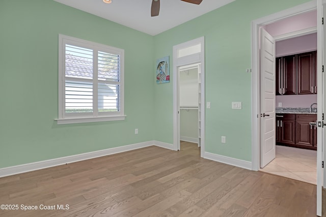 unfurnished bedroom featuring a closet, baseboards, a walk in closet, light wood-style floors, and ceiling fan