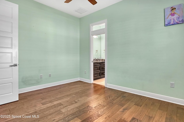unfurnished bedroom featuring wood finished floors, baseboards, visible vents, and connected bathroom