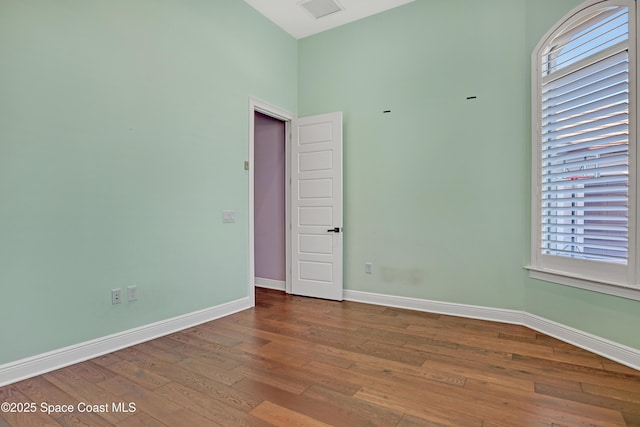 empty room with a towering ceiling, baseboards, hardwood / wood-style floors, and a healthy amount of sunlight