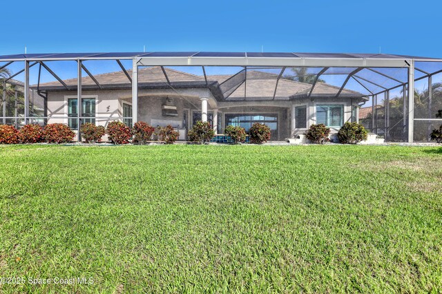 rear view of house featuring stucco siding, glass enclosure, and a lawn
