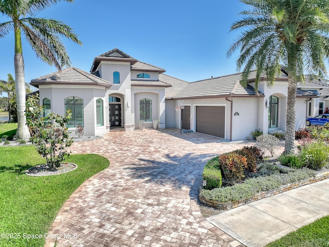 mediterranean / spanish-style house with stucco siding, decorative driveway, a tile roof, an attached garage, and french doors