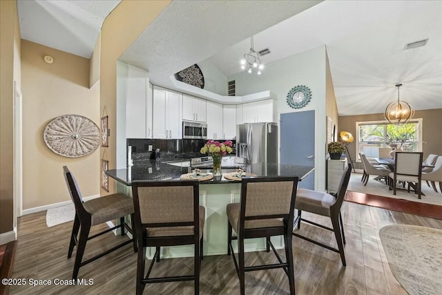kitchen with white cabinetry, appliances with stainless steel finishes, a peninsula, visible vents, and an inviting chandelier