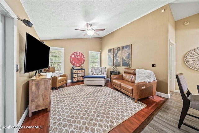 living area with lofted ceiling, baseboards, a textured ceiling, a ceiling fan, and wood finished floors