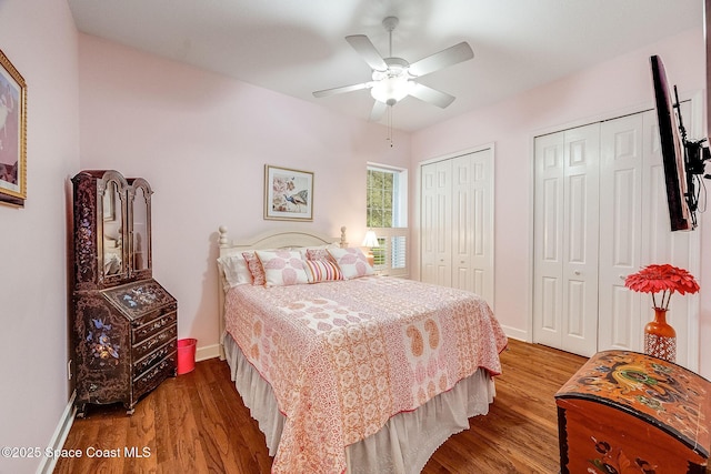 bedroom with wood finished floors, baseboards, a ceiling fan, and multiple closets