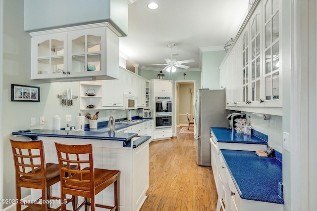 kitchen featuring a kitchen breakfast bar, ornamental molding, a peninsula, a ceiling fan, and appliances with stainless steel finishes
