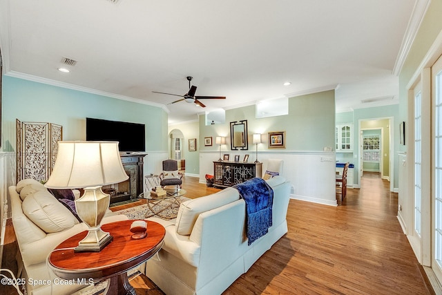 living area with arched walkways, a fireplace with flush hearth, crown molding, and wood finished floors