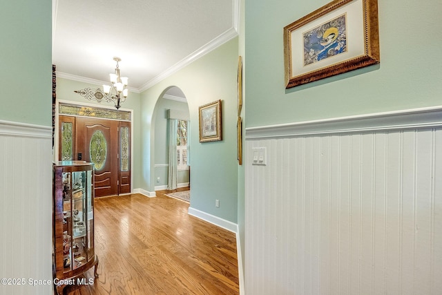 entryway featuring arched walkways, an inviting chandelier, crown molding, wainscoting, and wood finished floors