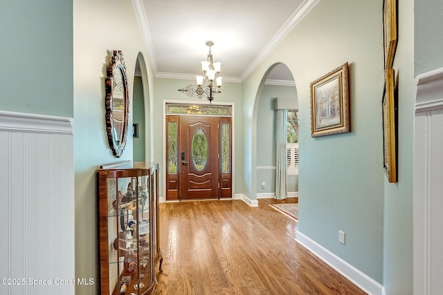 foyer featuring arched walkways, light wood finished floors, a notable chandelier, and ornamental molding