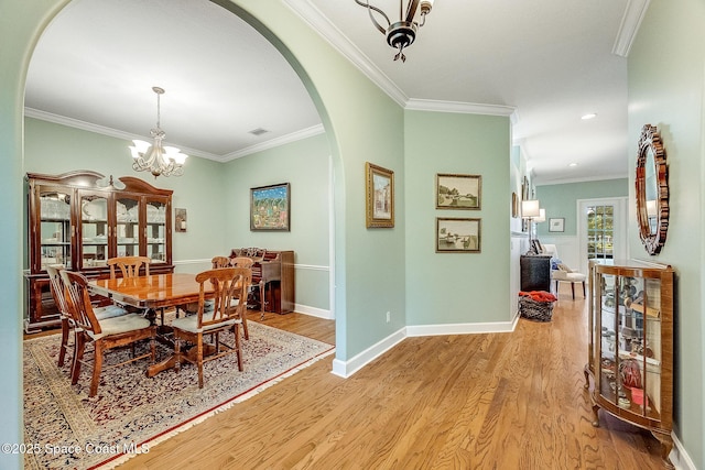 dining area with arched walkways, light wood-type flooring, ornamental molding, a notable chandelier, and baseboards