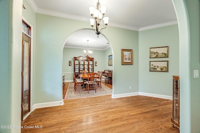 dining space with arched walkways, a notable chandelier, light wood-type flooring, and crown molding