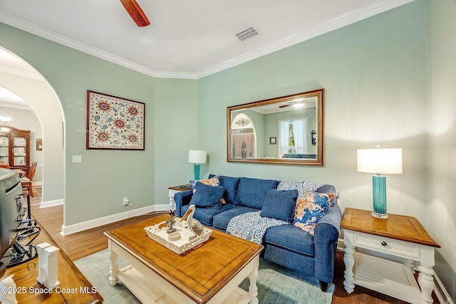 living area featuring arched walkways, ornamental molding, visible vents, wood finished floors, and baseboards