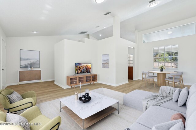 living room featuring light wood-type flooring, baseboards, lofted ceiling, and visible vents
