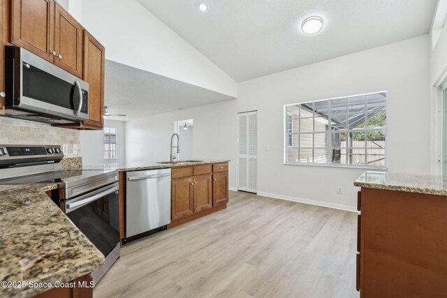 kitchen with tasteful backsplash, lofted ceiling, stainless steel appliances, a sink, and light stone counters