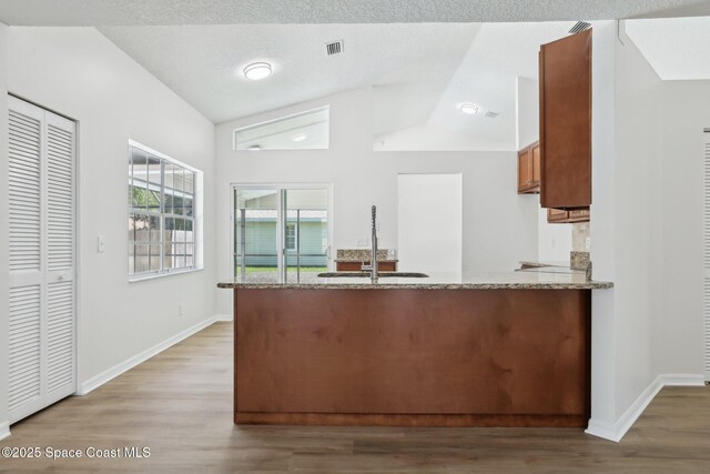 kitchen with vaulted ceiling, a sink, light wood finished floors, a peninsula, and brown cabinets