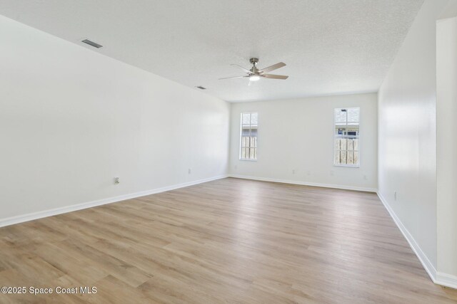 empty room featuring a ceiling fan, baseboards, light wood-style flooring, and visible vents