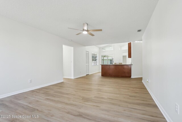 unfurnished living room with visible vents, baseboards, ceiling fan, lofted ceiling, and light wood-style floors