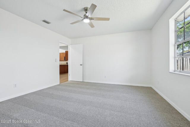 empty room featuring carpet flooring, baseboards, a textured ceiling, ceiling fan, and visible vents