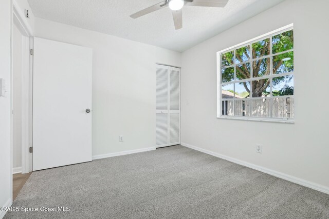 unfurnished bedroom featuring a closet, a textured ceiling, carpet, baseboards, and ceiling fan