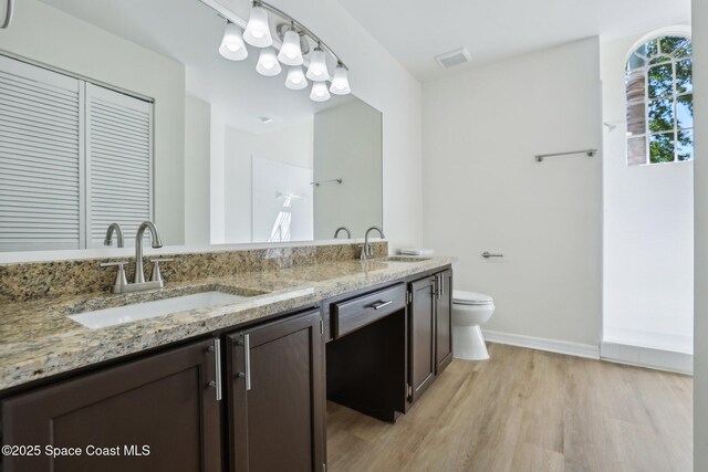 full bath featuring toilet, a sink, double vanity, and wood finished floors