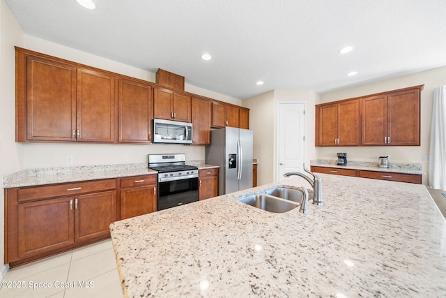 kitchen with recessed lighting, light stone counters, a sink, brown cabinetry, and appliances with stainless steel finishes