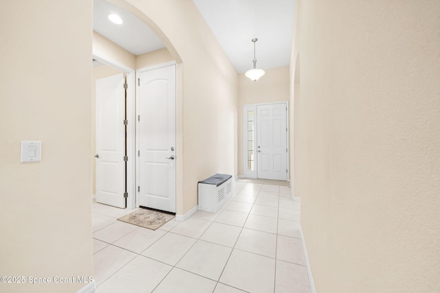 hall with baseboards, arched walkways, and light tile patterned floors