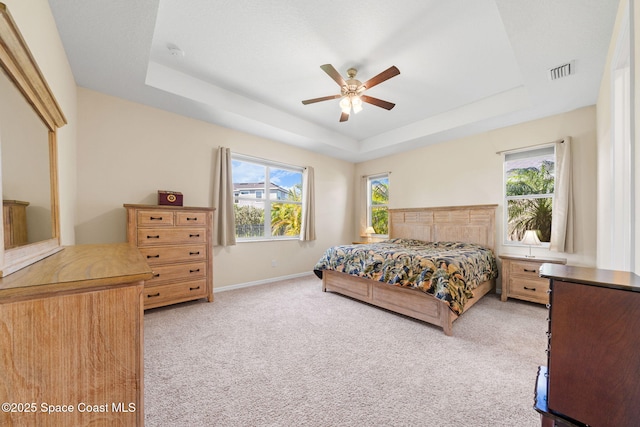 bedroom featuring light colored carpet, multiple windows, a tray ceiling, and visible vents