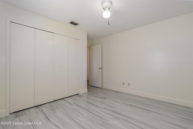 unfurnished bedroom featuring light wood-type flooring, baseboards, a textured ceiling, visible vents, and a closet