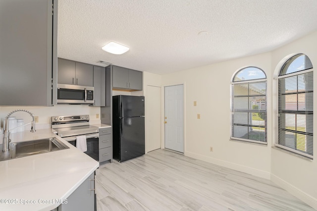 kitchen featuring light countertops, gray cabinets, stainless steel appliances, a sink, and light wood-style flooring