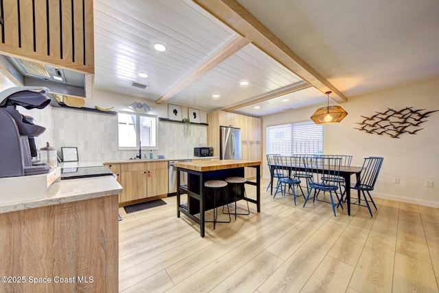 kitchen with a sink, appliances with stainless steel finishes, beam ceiling, and light wood-type flooring