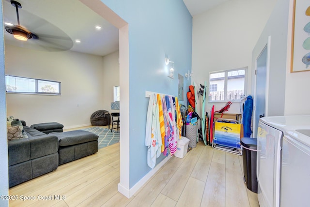recreation room featuring wood finished floors, baseboards, ceiling fan, a high ceiling, and separate washer and dryer