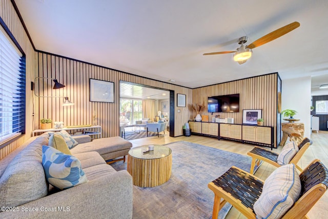 living room featuring a ceiling fan, wood finished floors, a wealth of natural light, and wood walls
