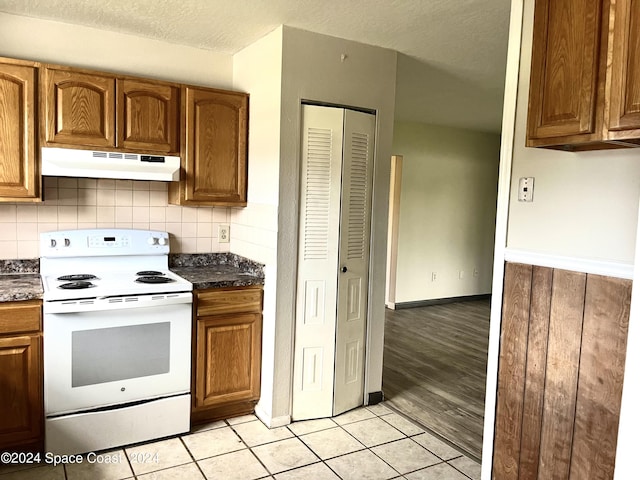 kitchen featuring a textured ceiling, white electric range oven, under cabinet range hood, light tile patterned floors, and dark countertops