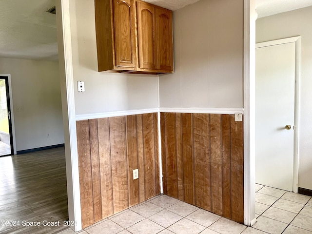 interior space featuring wainscoting, light tile patterned floors, wooden walls, and brown cabinets