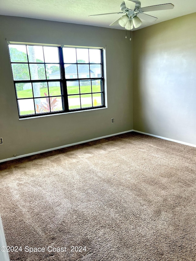 carpeted spare room featuring baseboards and a ceiling fan