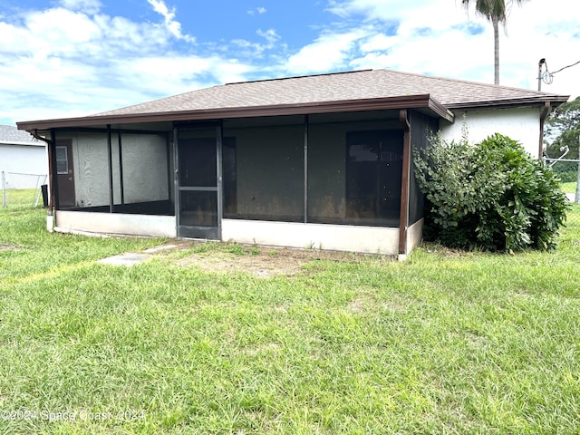 rear view of property with a lawn, a shingled roof, a sunroom, and stucco siding
