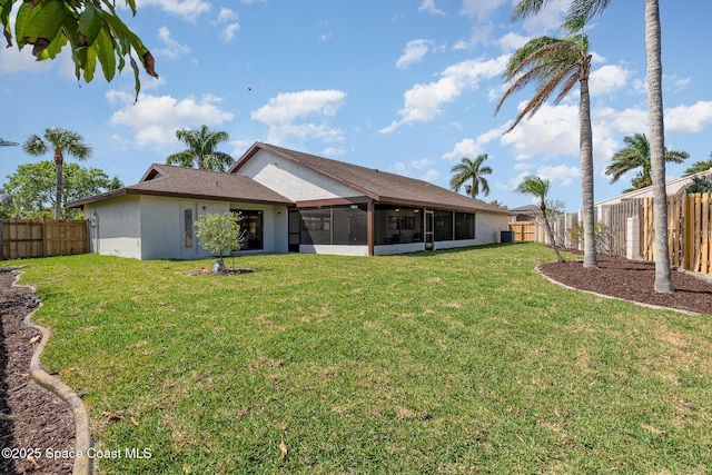 rear view of house featuring a fenced backyard, a lawn, stucco siding, and a sunroom