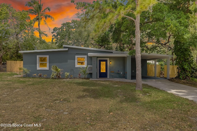 mid-century inspired home with fence, concrete driveway, stucco siding, a carport, and a lawn