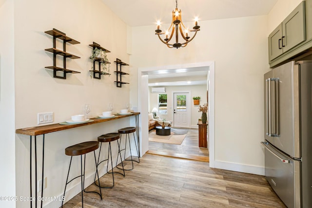 interior space with a breakfast bar, light wood-type flooring, high end fridge, an inviting chandelier, and baseboards