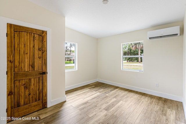 empty room with baseboards, a wall unit AC, a healthy amount of sunlight, and wood finished floors