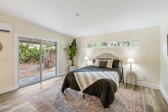 bedroom featuring baseboards, access to outside, an AC wall unit, and wood finished floors