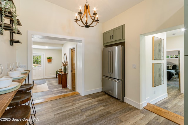 interior space featuring baseboards, light wood-style floors, a chandelier, and a high ceiling