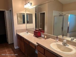 full bathroom with a stall shower, double vanity, a sink, and tile patterned floors