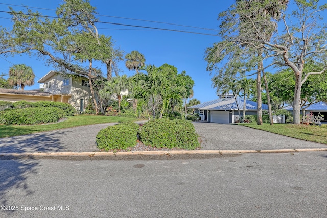 view of property hidden behind natural elements featuring decorative driveway, an attached garage, and a front lawn