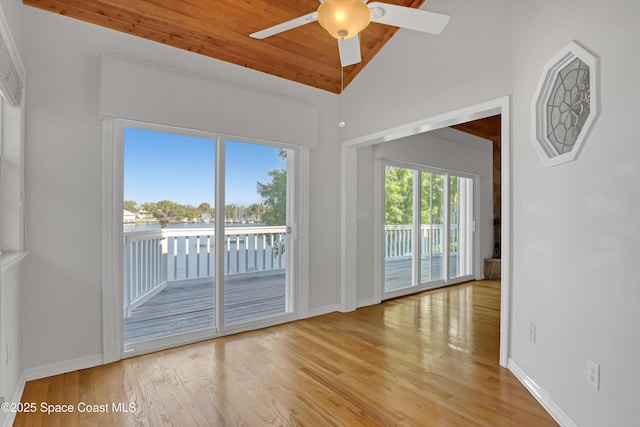 unfurnished room with lofted ceiling, ceiling fan, wood finished floors, a water view, and baseboards